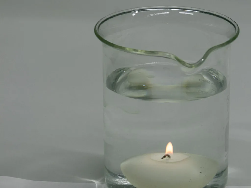 Brennende Kerze in einem mit Wasser gefüllten Becherglas.